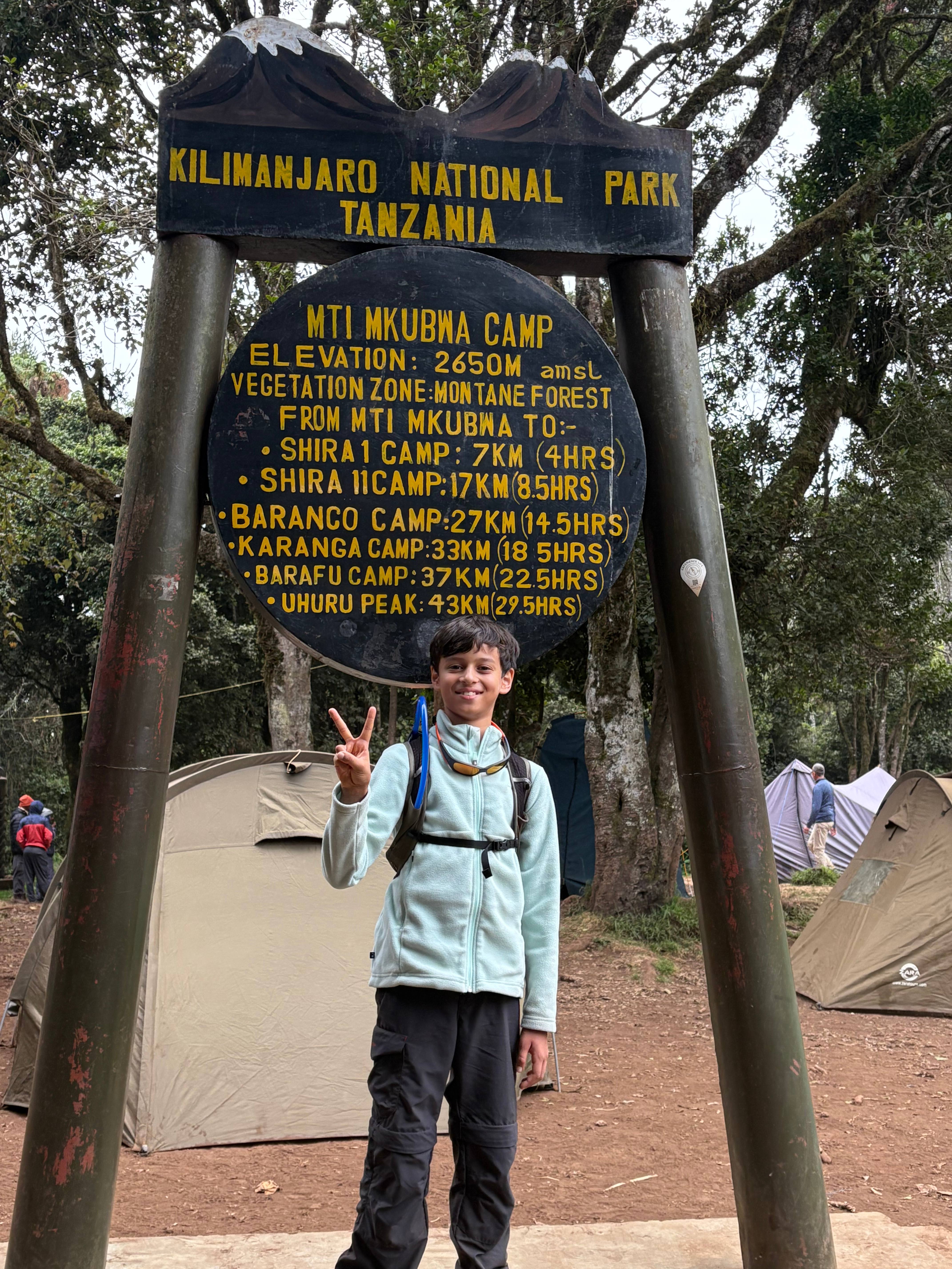 Standing at Mti Mkubwa Camp sign showing elevation and camp information